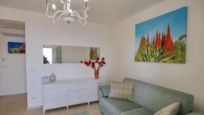 A living room with a green sofa, a white console table, a chandelier, and a painting of red flowers.