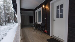 Un porche de madera con una puerta y ventana blancas, una pequeña mesa con sillas y el suelo cubierto de nieve.