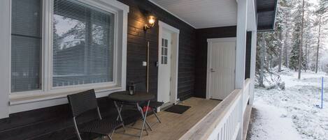 A covered porch with a wooden table and chairs, a lantern, and a door.