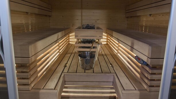 Una sauna con bancos de madera y un banco central con un cubo de metal.
