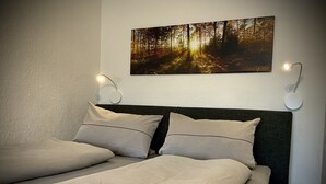 Ein Schlafzimmer mit einem Bett, zwei Wandleuchten und einem Wandbild mit Waldmotiv.