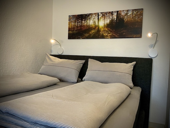 A bedroom with a bed, two wall-mounted lights, and a forest-themed painting.