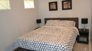Quarto com cama, duas mesas de cabeceira e duas luminárias fixadas na parede.