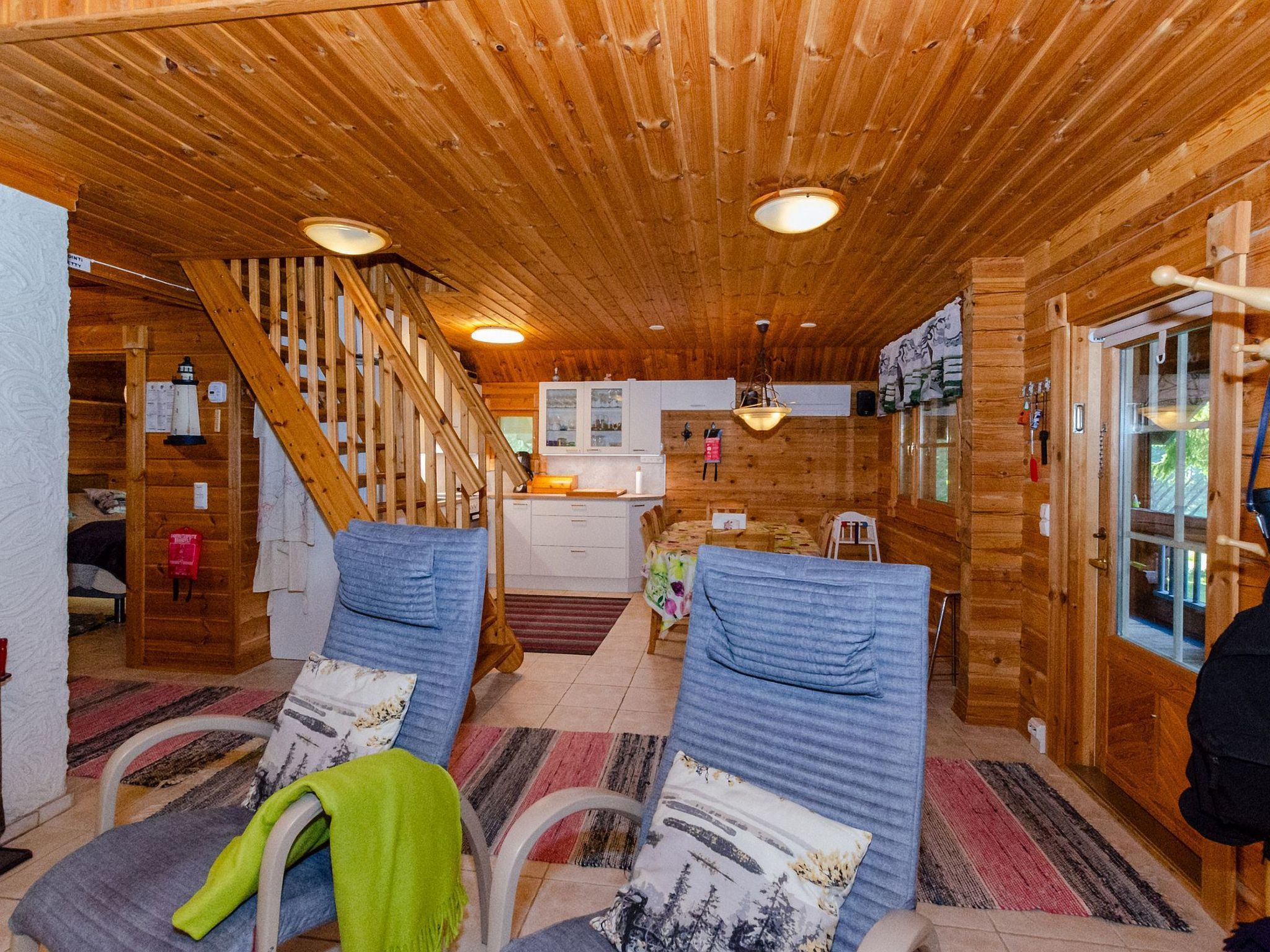 A wooden cabin interior with a staircase, a kitchen area, and two chairs with cushions.