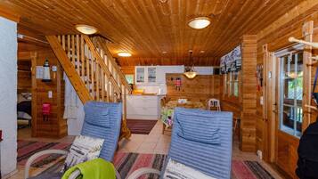 A wooden cabin interior with a staircase, a kitchen area, and two chairs with cushions.