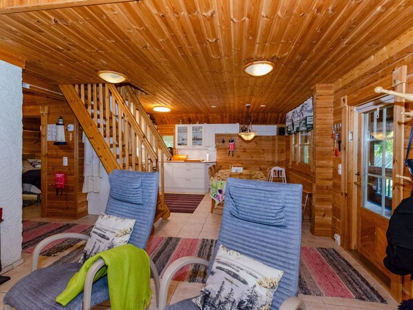 A wooden cabin interior with a staircase, a kitchen area, and two chairs with cushions.