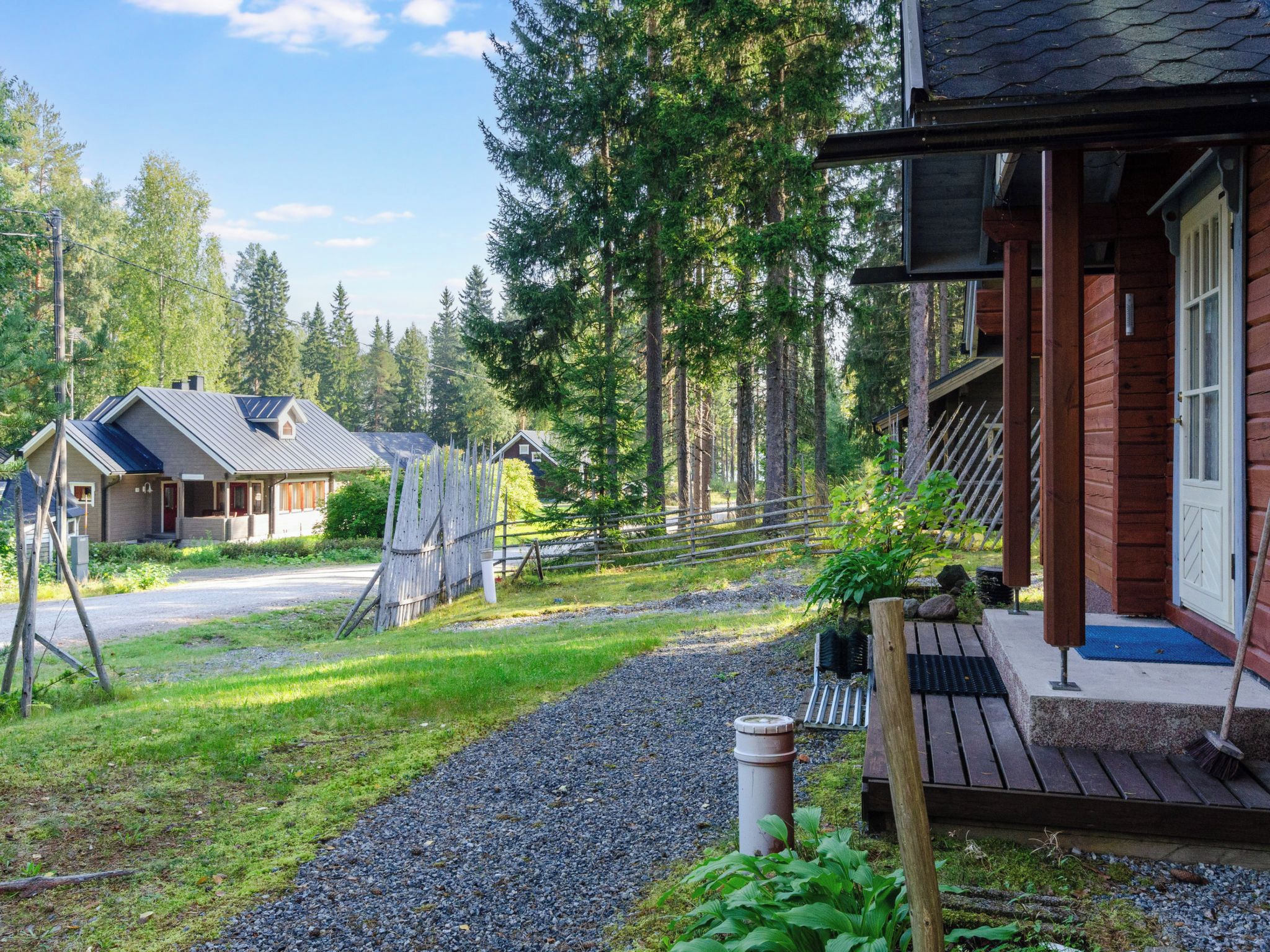 A wooden cabin with a porch, surrounded by a gravel path and a wooden fence.