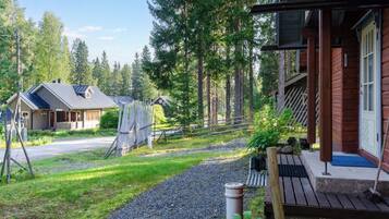 A wooden cabin with a porch, surrounded by a gravel path and a wooden fence.