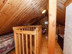 Quarto de sótão com pé direito inclinado, rodapé de madeira e cama com roupa de cama floral.