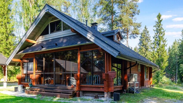 Mökki, jossa on suuri kuisti, katettu terassi ja näkymä ympäröivään metsään.