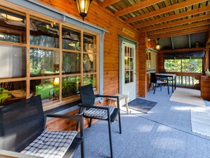 A wooden cabin with a porch, a dining table, and chairs.