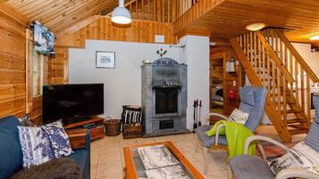 A cozy log cabin interior with a television, fireplace, wooden staircase, and comfortable seating.