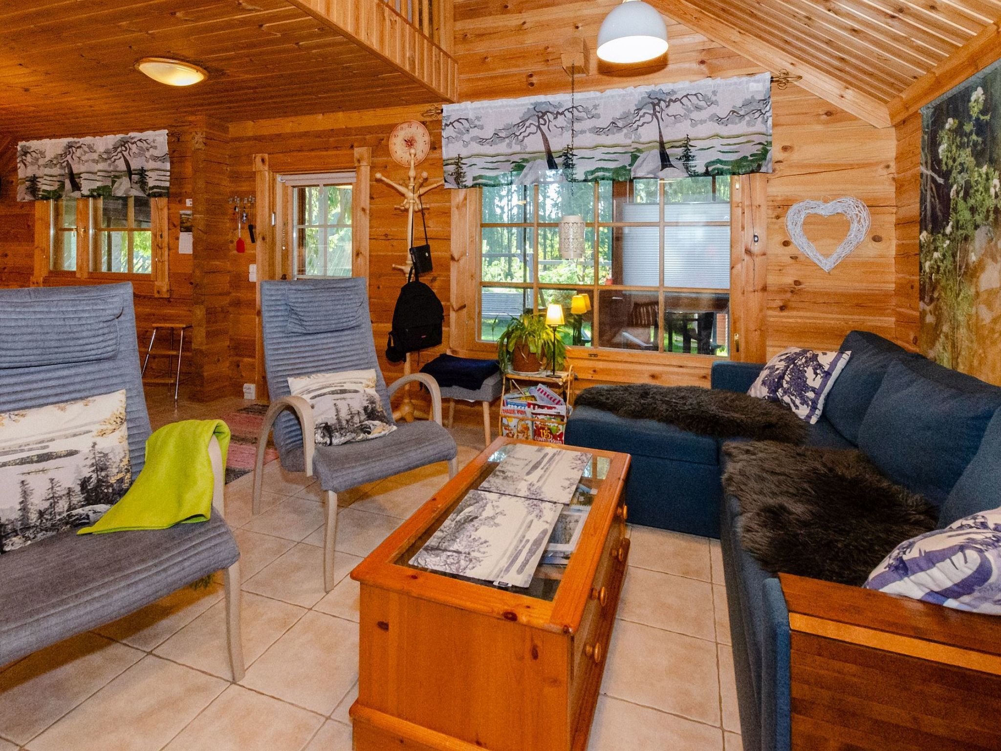 Ein gemütliches Cabin-Interieur mit Holzbalkendecke, einer Couch, einem Sessel, einem kleinen Tisch und einem Fenster mit Blick auf Bäume.
