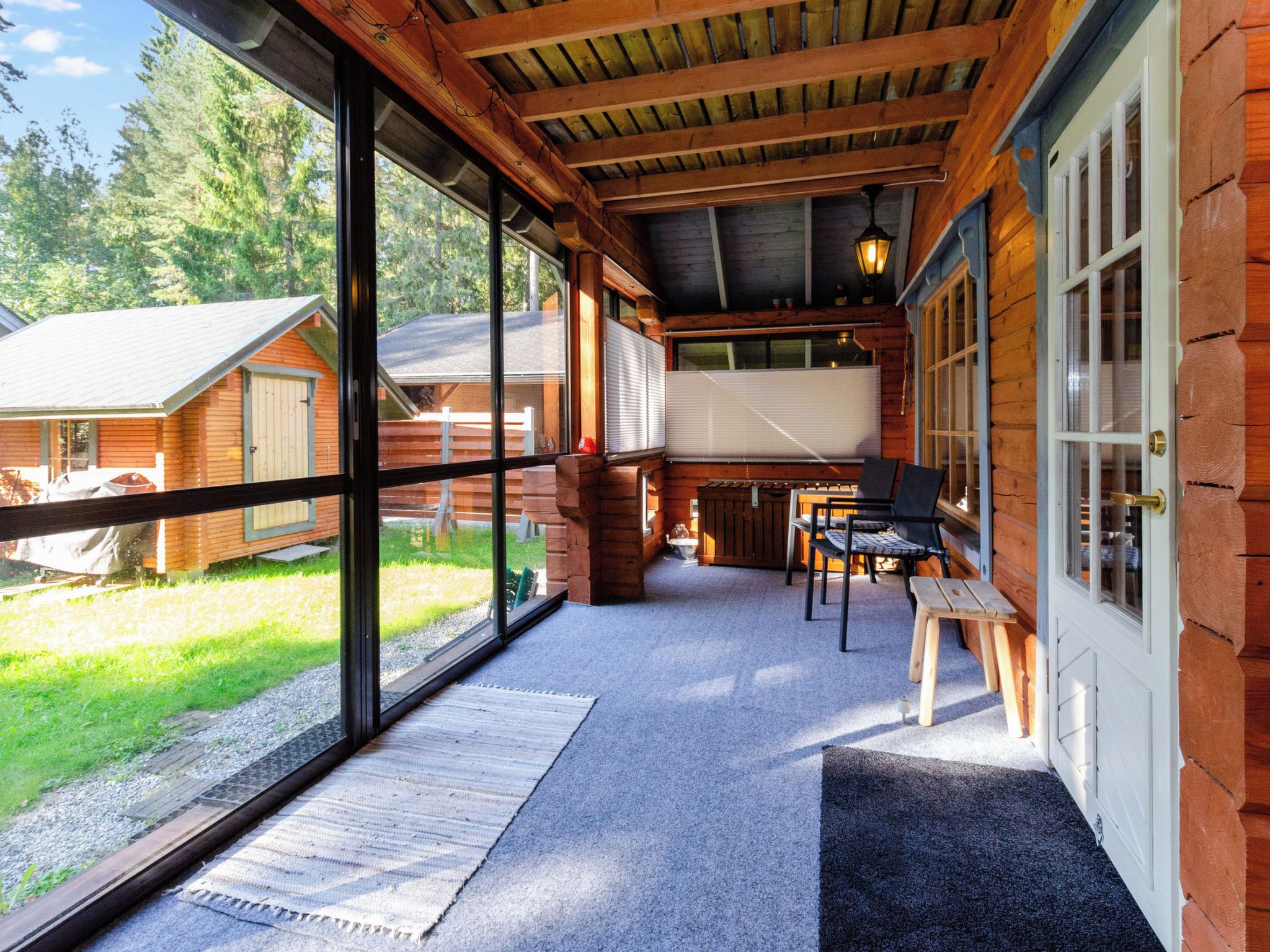 Eine überdachte Veranda mit Blick auf eine Holzhütte, ein Tisch mit Stühlen und eine Bank.
