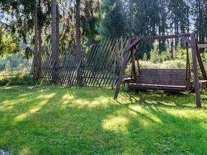 A wooden swing set in a grassy area with a wooden fence and trees in the background. - Purnukka by Interhome (Lieksa)