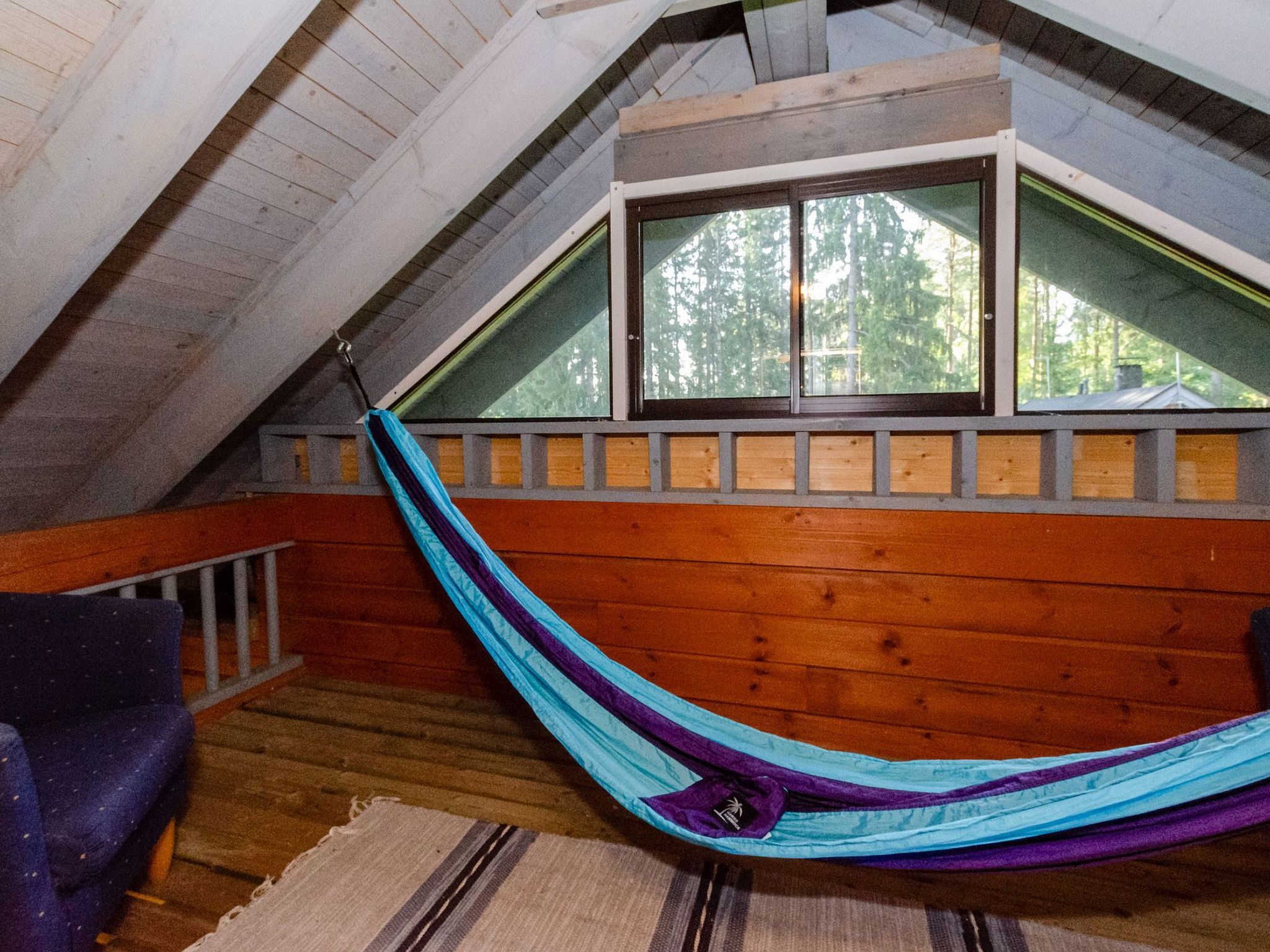 Eine Hängematte in einem Schlafzimmer unter dem Dach mit Holzboden und einem Fenster mit Blick auf Bäume.