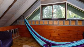 Eine Hängematte in einem Schlafzimmer unter dem Dach mit Holzboden und einem Fenster mit Blick auf Bäume.