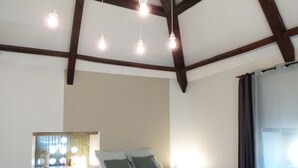 Une chambre avec un plafond en bois, un lit avec une literie blanche, une table de chevet et une fenêtre avec des rideaux.