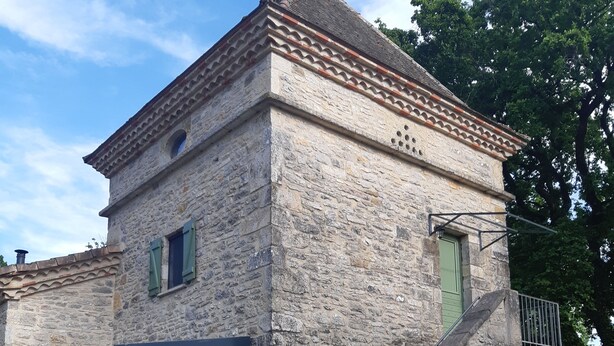 Un bâtiment en pierre doté d’un toit traditionnel recouvert de tuiles, d’une entrée fermée par des panneaux de verre et d’un petit escalier menant à une porte.