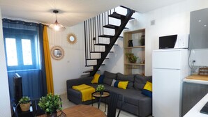 Un espace de vie compact comprenant un canapé, une table à manger, des chaises, un escalier et un coin cuisine.