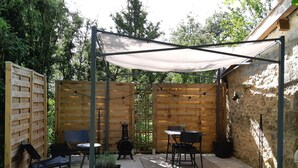 Un patio couvert avec des murs en bois, deux tables avec des chaises, une plante en pot et un barbecue.
