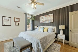 A bedroom with a bed, bedside tables, a bench, a ceiling fan, and a wall-mounted painting. - The Classy Craftsman - Beautiful Decor & Pool (Atlanta)