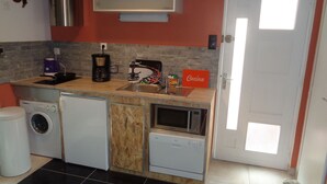 Ett kompakt kök med tvättmaskin, kaffebryggare, mikrovågsugn och ett litet kylskåp.