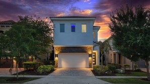 A modern two-story house with a garage, surrounded by well-maintained landscaping and trees. - Modern Luxury Villa | 5BR, 5 Bath Luxe Home w/ Private Pool, Arcade, and Theater Near Disney (Kissimmee)