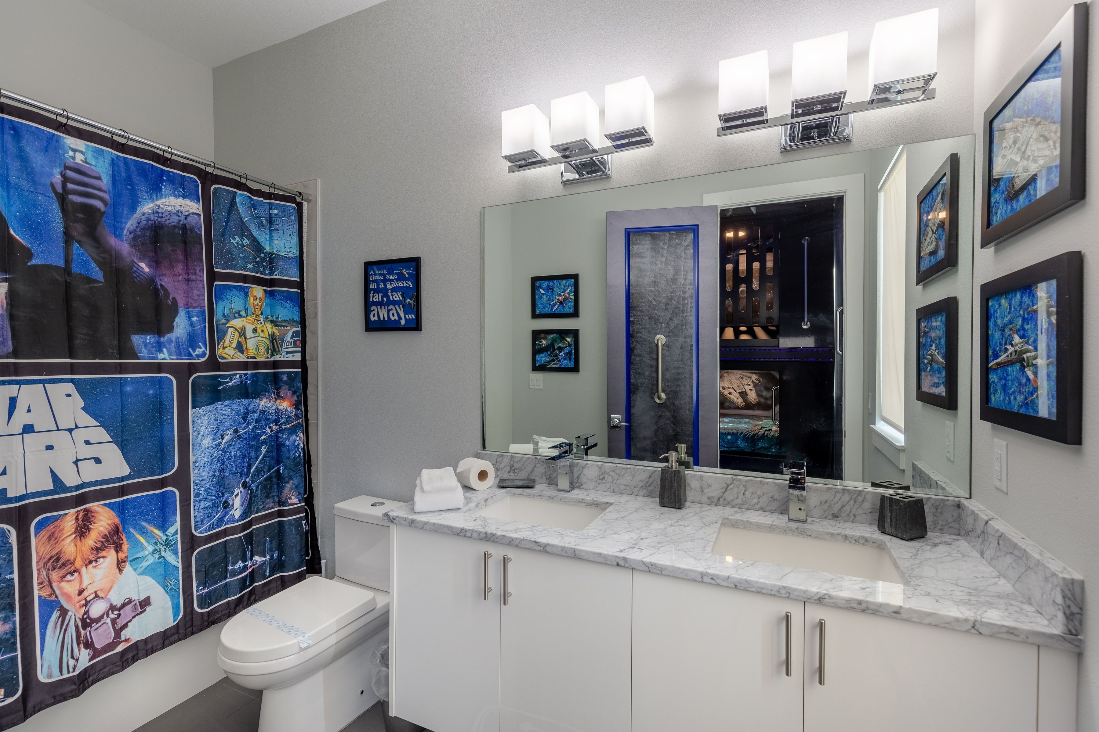 A modern bathroom with a Star Wars themed shower curtain, a large mirror, and a marble sink.