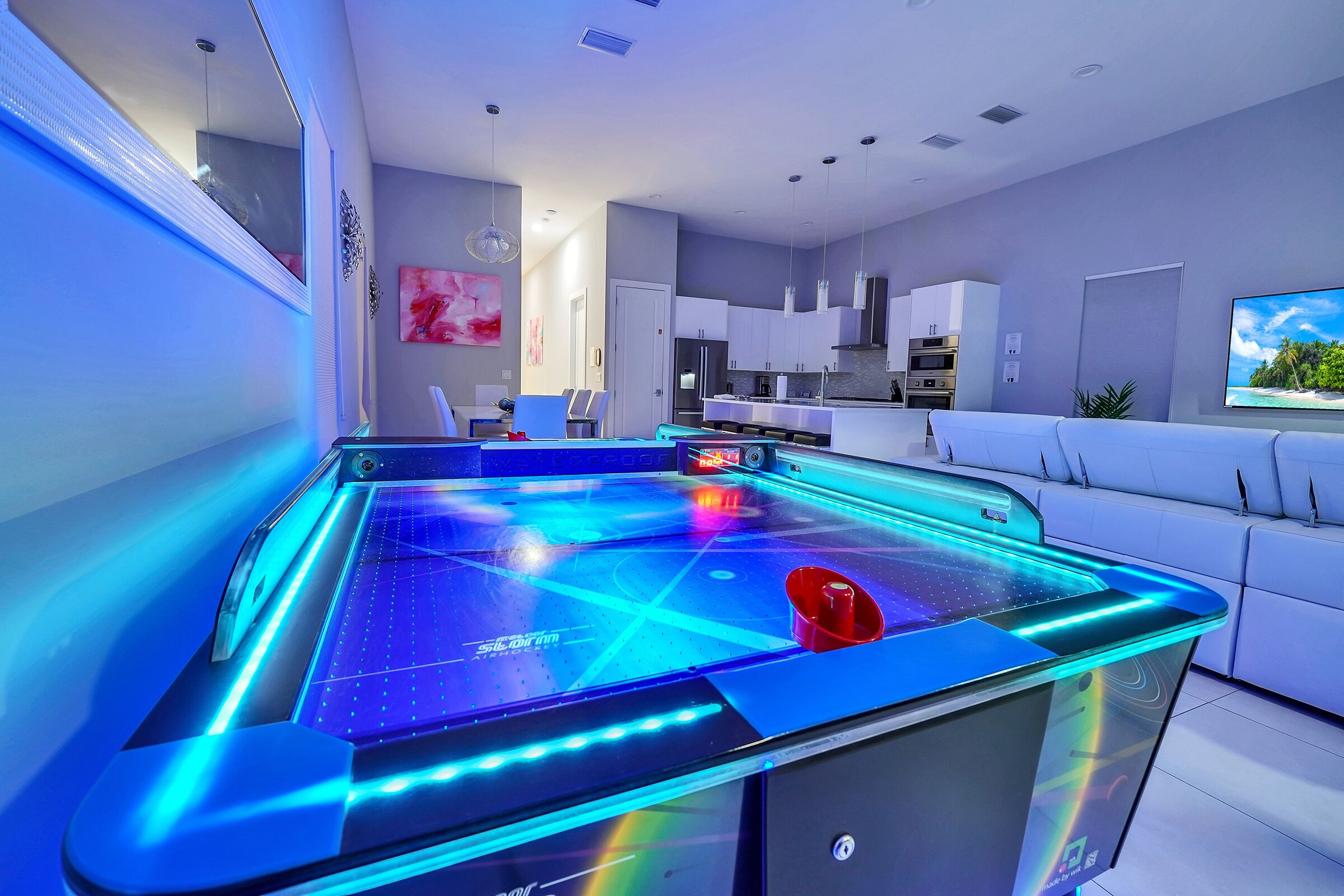 A modern living room with a large, illuminated pool table, a sofa, and a kitchen area in the background.