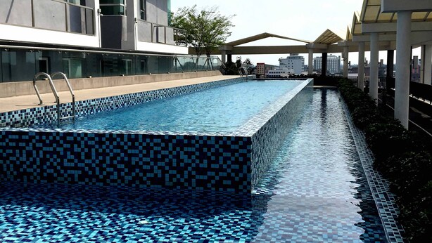A modern outdoor swimming pool with a checkered tile design, surrounded by a covered walkway and a building with large windows. - Excellent Location Premium Studio @ Palo 101 Ipoh (Kampung Jawa)