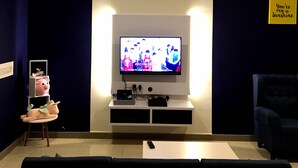 A living room with a television mounted on the wall, a small table with a pig-shaped lamp, a blue armchair, and a yellow sign on the wall. - Excellent Location Premium Studio @ Palo 101 Ipoh (Kampung Jawa)