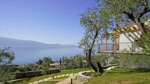 A hillside property with a stone pathway leading to a building with a balcony overlooking a body of water. - lake view apartment quiet location parking and swimming pool in the olive trees. (Gargnano)