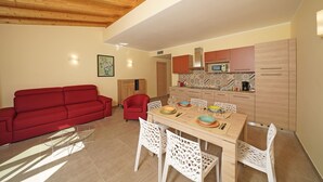 A modern living room with a red sofa, a dining table with chairs, and a kitchen area with wooden cabinets and a microwave. - lake view apartment quiet location parking and swimming pool in the olive trees. (Gargnano)