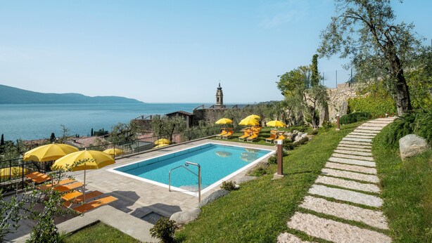 A pool area with a stone pathway, yellow umbrellas, and a view of the sea. - lake view apartment quiet location parking and swimming pool in the olive trees. (Gargnano)