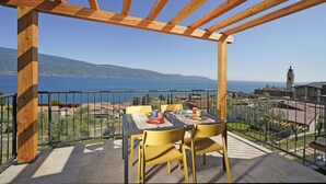 A balcony with a wooden pergola, a table with chairs, and a view of the sea and buildings. - lake view apartment quiet location parking and swimming pool in the olive trees. (Gargnano)