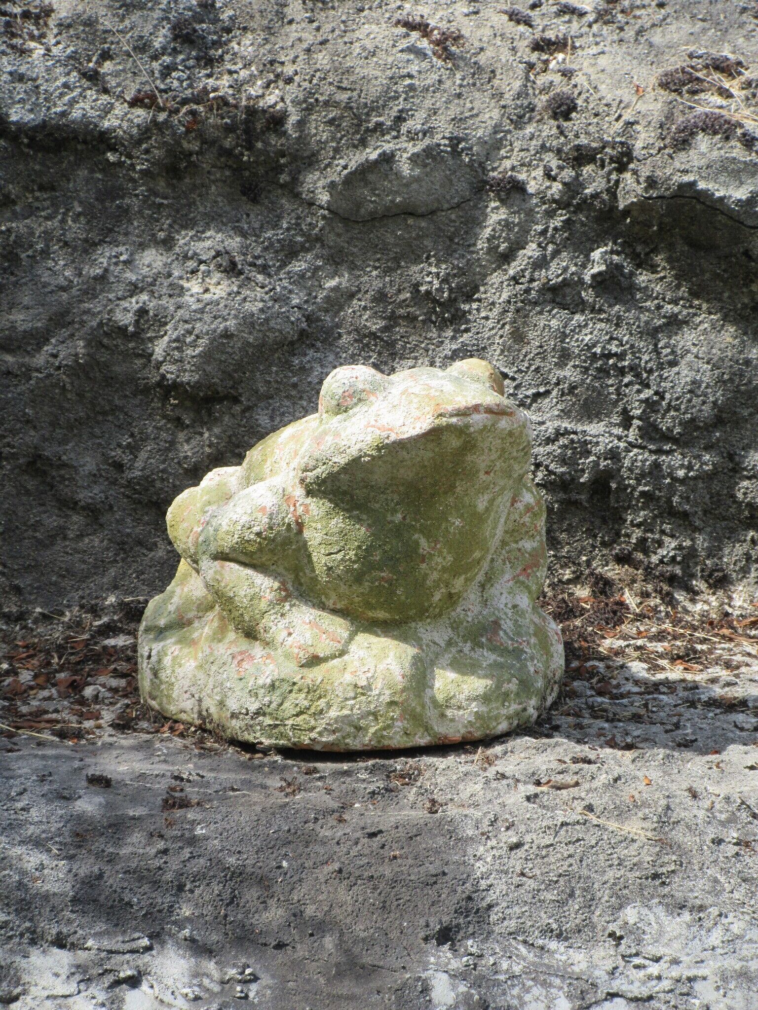 Eine steinerne Skulptur mit rauer Oberfläche und Moosbewuchs vor felsigem Hintergrund.