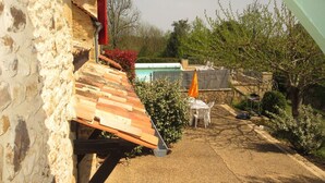 Un edificio in pietra con tetto spiovente, una piscina e un patio con mobili da esterno.