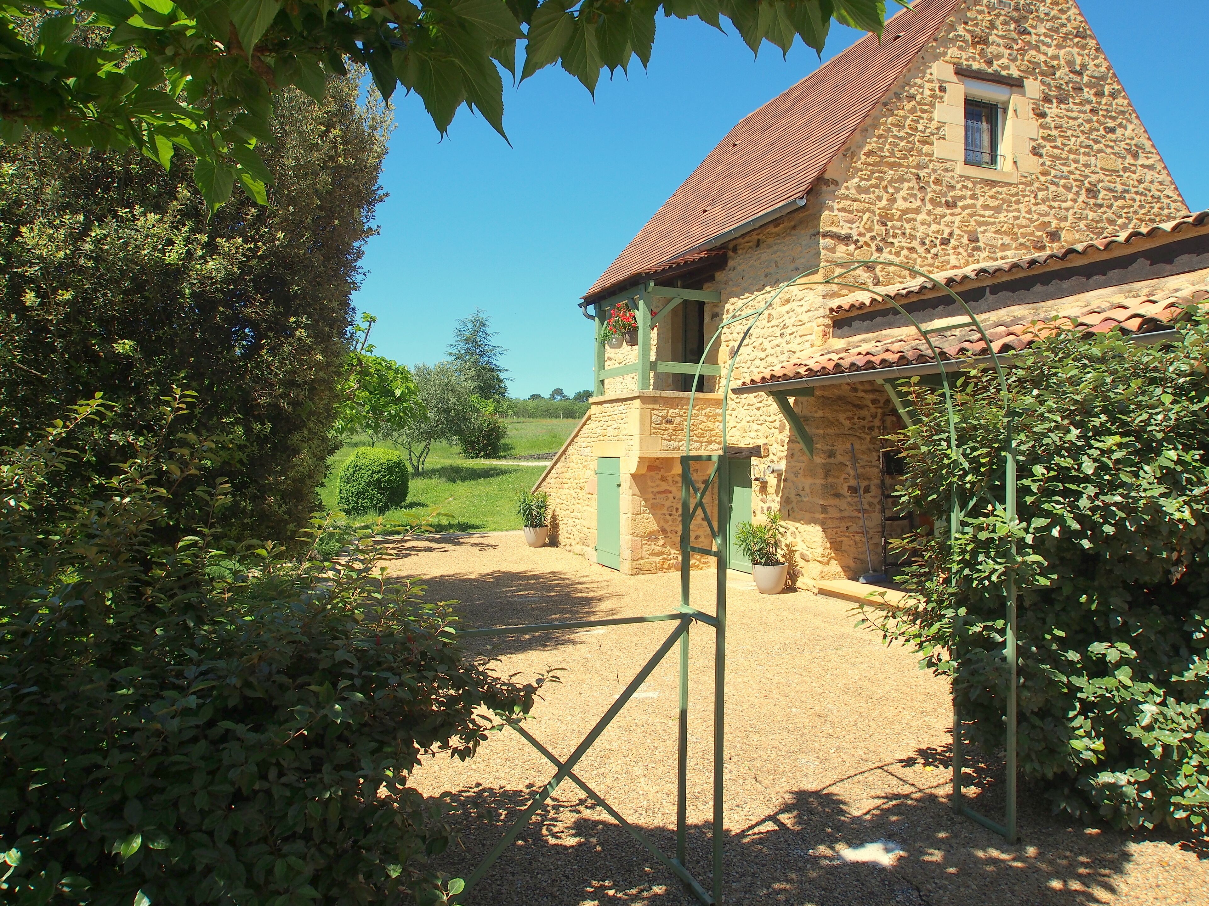 A stone building with a tiled roof, a gravel path, and surrounding greenery.