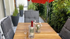 Ein Holztisch mit zwei Stühlen, einer Champagnerflasche, zwei Gläsern und einer Blumenvase.