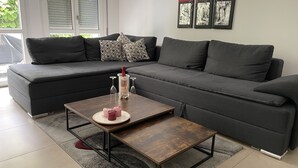 Ein modernes Wohnzimmer mit einem dunkelgrauen Ecksofa, einem Holztisch und einem Glaskaraffel.