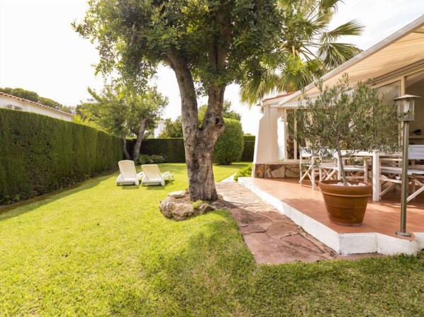 A well-maintained backyard with a lawn, two lounge chairs, a large potted tree, and a patio area with outdoor furniture. - La sorpresa by Interhome (Cambrils)