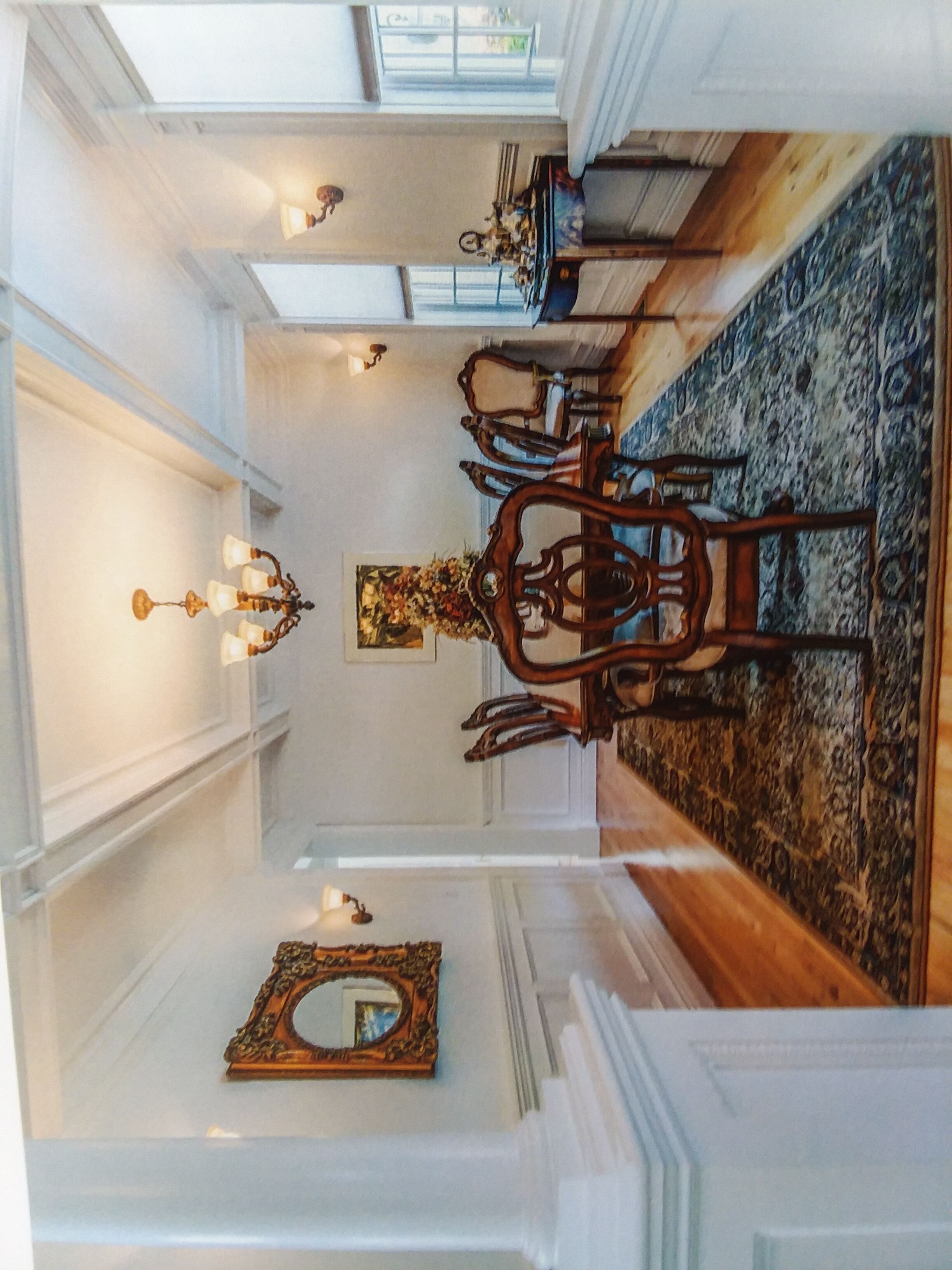 A dining area with a wooden dining table and chairs, a chandelier, and a mirror on the wall.