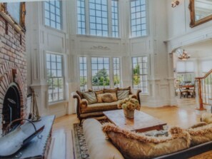 A spacious room with a large fireplace, a cozy sofa set, and a dining area visible through large windows. - Southampton watermill estate   $3900.00 per night (Water Mill)