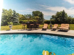 A swimming pool with lounge chairs and a table, surrounded by greenery.