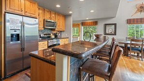 A modern kitchen with wooden cabinets, stainless steel appliances, a granite countertop, and a bar area with stools. - Ping Pong, Foosball, Pet Friendly, Mountain Living (Durango)