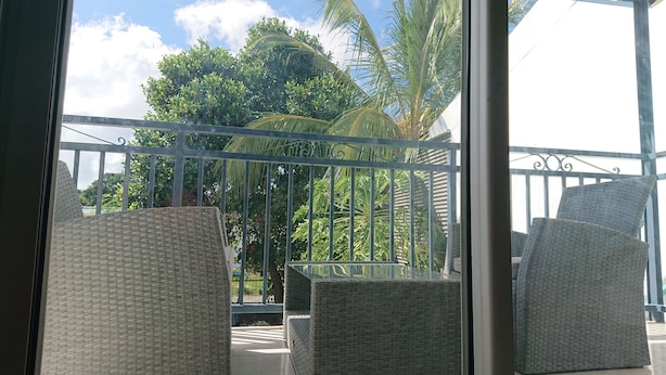 Un balcón con mobiliario de mimbre y vistas a exuberante follaje y palmeras.