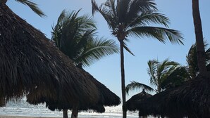 A beachside restaurant with thatched umbrellas, plastic chairs, and tables.