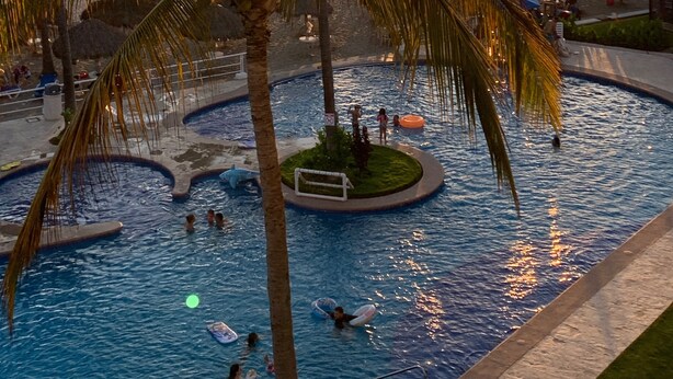 A swimming pool with palm trees and a sunset in the background.
