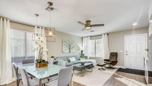 Ein modernes Wohnzimmer mit einem Glastisch, grauen Stühlen, einer Couch und einem Deckenventilator.